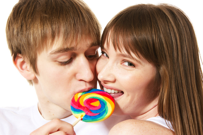A young teenage couple shares a lollipop